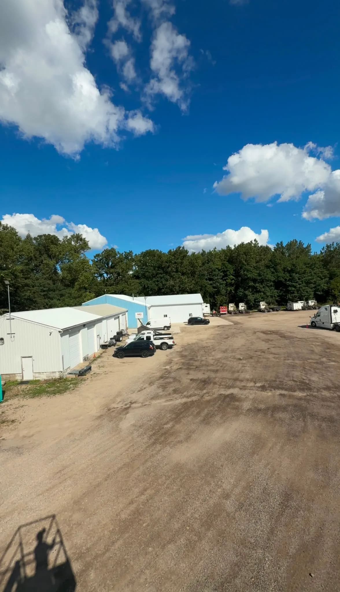 The Holt Rd yard beside Building C Warehouse 1, with trucks and trailers parked along the tree line